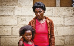 African woman and girl standing by a wall.