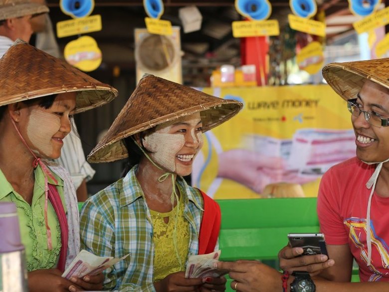 Men and women in Myanmar. using the Wave Money cellphone application for financial transactions.